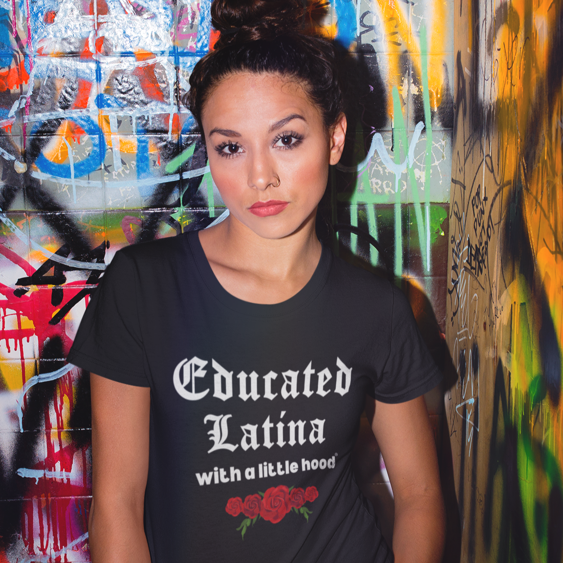 Woman wearing 'Educated Latina with a Little Hood' t-shirt, graffiti background.