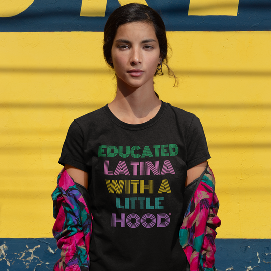 Woman wearing a black t-shirt with colorful text that says 'Educated Latina with a Little Hood' in front of a yellow and blue background