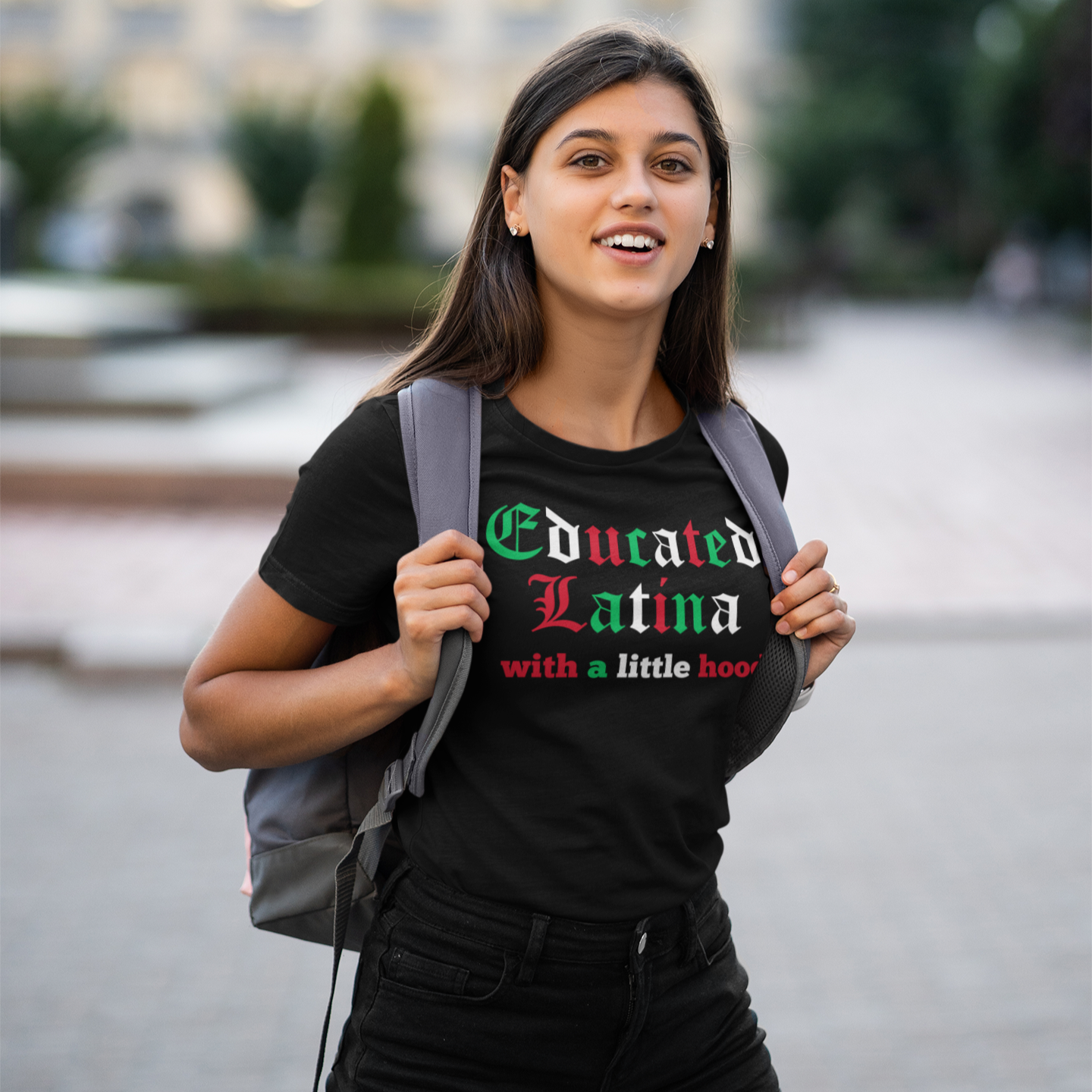 Woman wearing a black t-shirt with 'Educated Latina with a little hood' text, standing outdoors.
